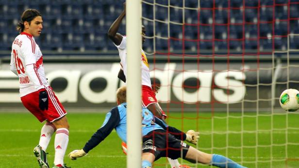 Ein Fußballspieler von Red Bull Salzburg schießt ein Tor, während der Torwart versucht, den Ball abzuwehren.