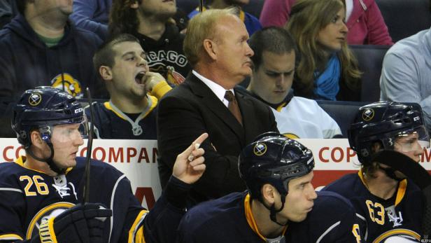 Ein Trainer der Buffalo Sabres steht hinter zwei Spielern auf der Bank.