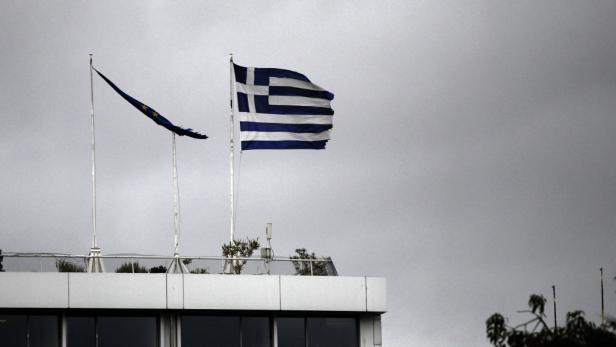 Die griechische und die EU-Flagge wehen beschädigt auf einem Gebäude.