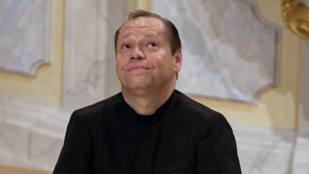 Ein Mann in schwarzem Hemd blickt lächelnd nach oben.