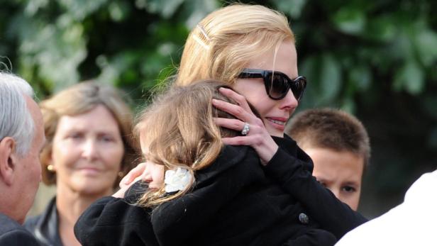 Nicole Kidman umarmt ein Kind, während andere Personen im Hintergrund stehen.