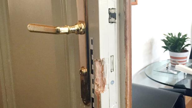 Eine beschädigte Tür mit einem goldenen Türgriff und Spuren von Reparaturarbeiten.