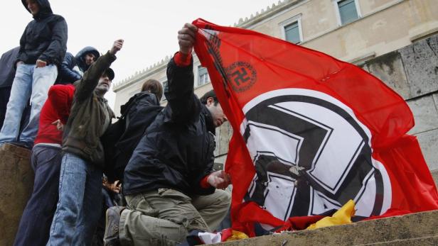 Eine Gruppe von Menschen hält eine rote Flagge mit einem Hakenkreuz hoch.