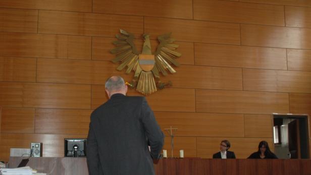 Ein Mann steht vor einer hölzernen Wand mit dem österreichischen Bundesadler.