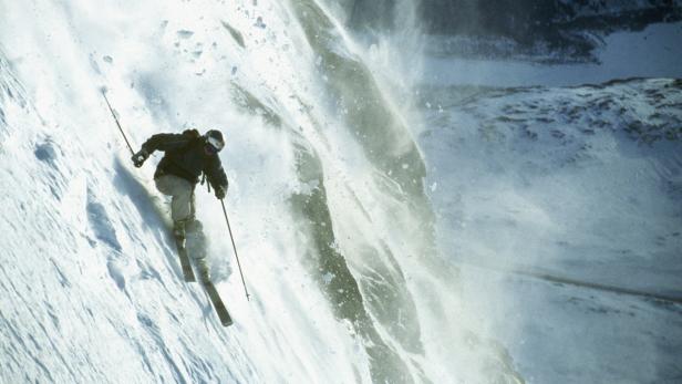 Ein Skifahrer fährt einen steilen Hang hinunter, umgeben von aufgewirbeltem Schnee.