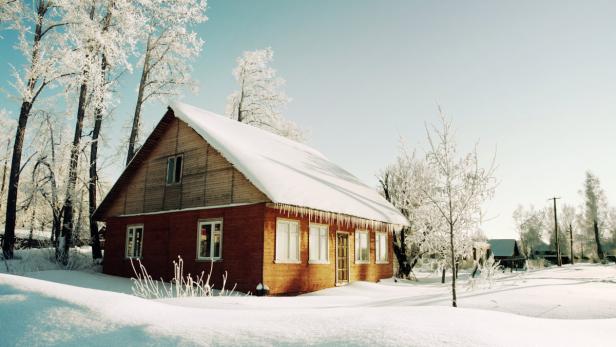 Snowy hills in Russian countryside in morning. Red wooden house windows turned to east.