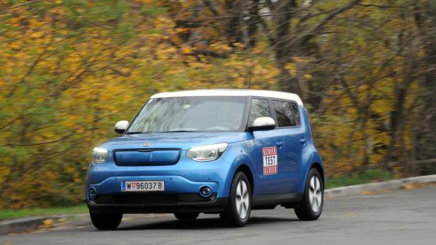 Ein blauer Kia Soul fährt auf einer Straße mit Bäumen im Hintergrund.