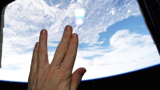 Eine Hand vor einem Fenster mit Blick auf die Erde aus dem Weltraum.