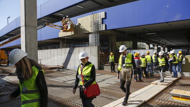 Mehrere Bauarbeiter mit Schutzhelmen und Warnwesten auf einer Baustelle.