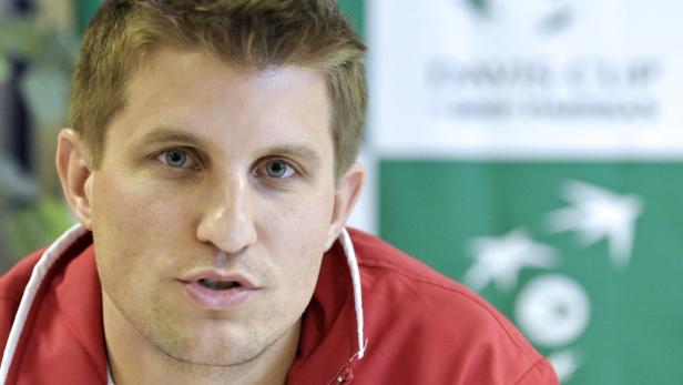 Ein Mann mit blonden Haaren und blauen Augen in einem roten Hemd vor einem grünen Hintergrund.