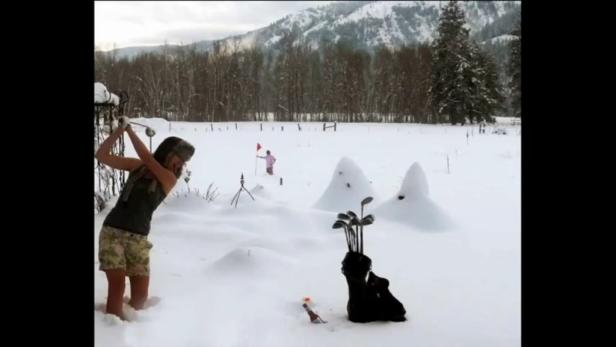 Eine Frau spielt Golf im Schnee, während eine andere Person eine rote Flagge hält.