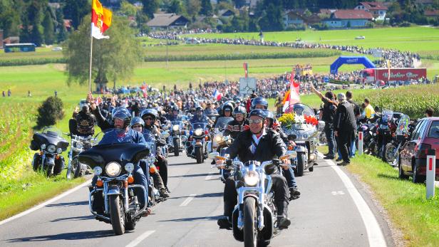 Eine Parade von Motorradfahrern fährt eine Landstraße entlang.