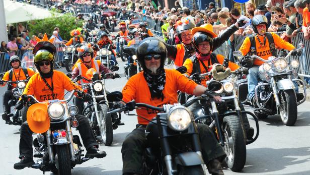 Eine Parade von Motorradfahrern in orangefarbenen Hemden fährt durch eine Menschenmenge.