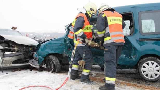 Zwei Feuerwehrleute arbeiten an einem verunglückten Auto.