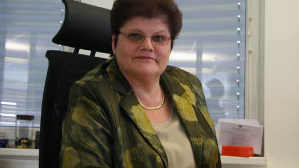 Eine Frau mit Brille sitzt an einem Schreibtisch vor einem Fenster.