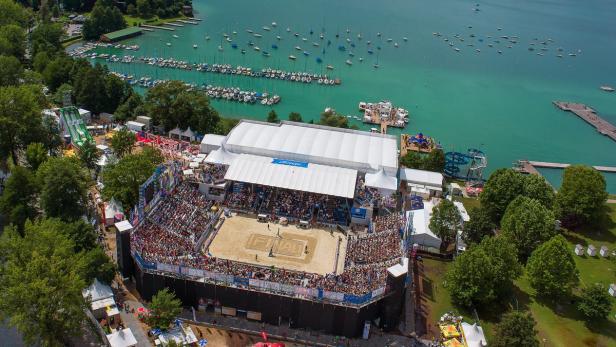 Luftaufnahme eines Beachvolleyballturniers am See mit Zuschauern und Booten.