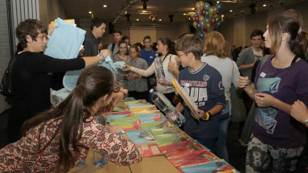 Eine Gruppe von Menschen steht an einem Tisch mit bunten Dokumenten und erhält Gegenstände.