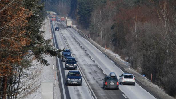 Autos und LKW fahren auf einer leicht verschneiten Autobahn durch eine winterliche Landschaft.