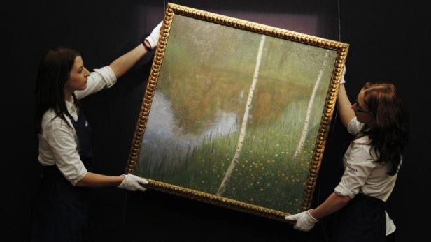 zwei personen halten ein gemälde Klimts "Seeufer" um 6,7 Mio. Euro verkauft