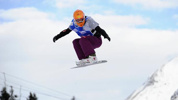 Ein Snowboarder springt in der Luft vor einem verschneiten Berghang.
