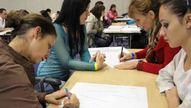 Mehrere Frauen sitzen an Tischen und füllen Arbeitsblätter aus.