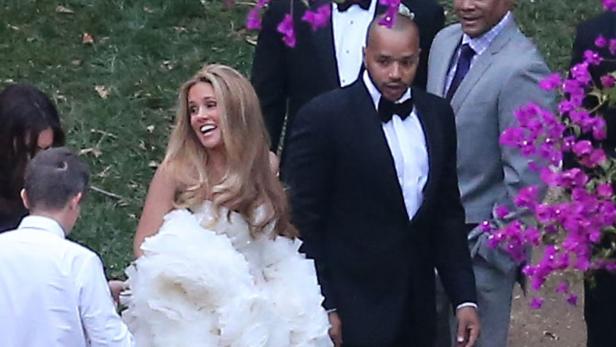 Eine lächelnde Braut in einem weißen Kleid mit einem Mann im Smoking bei einer Hochzeit.