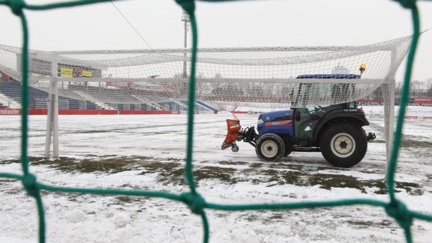 Ein Traktor mit Schneepflug räumt einen Fußballplatz von Schnee frei.