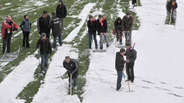 Eine Gruppe von Menschen schaufelt Schnee von einem Fußballfeld.