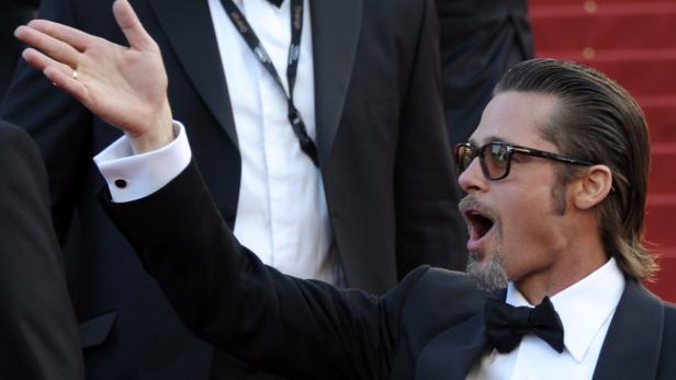 Brad Pitt gestikuliert auf einem roten Teppich.