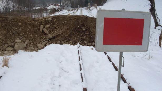 Eine rote Warntafel steht vor einer blockierten Eisenbahnstrecke im Schnee.