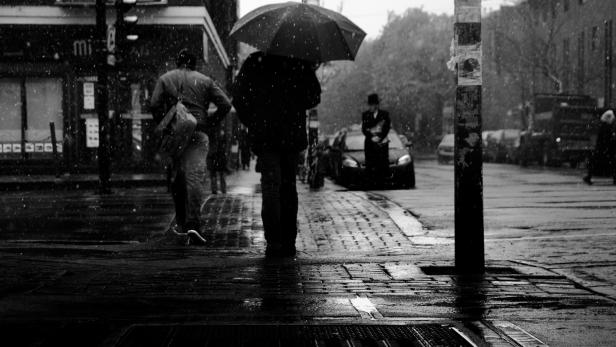 Ein regnerischer Tag in der Stadt, Menschen mit Regenschirmen eilen vorbei.
