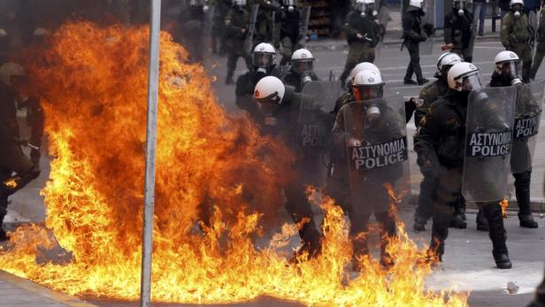 Polizisten in Schutzkleidung stehen vor einem Feuer auf der Straße.