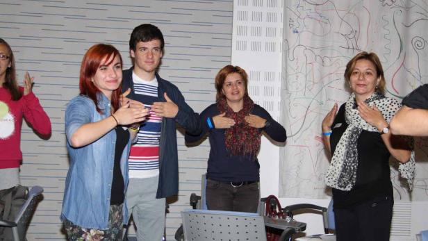 Eine Gruppe von Menschen steht in einem Raum und hält die Hände auf die Brust.