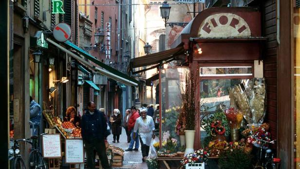 Eine belebte Gasse mit Geschäften und Passanten in einer italienischen Stadt.