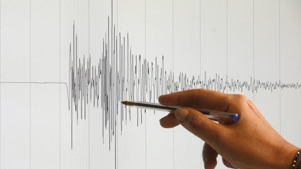 Eine Hand deutet mit einem Stift auf eine seismografische Aufzeichnung.