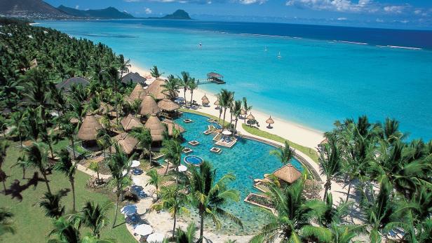 Ein tropisches Resort mit Palmen, strohgedeckten Hütten und einem großen Pool am Strand.