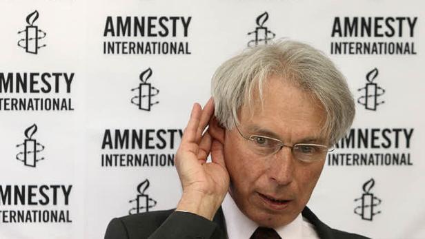 Ein Mann mit Brille posiert vor einem Hintergrund mit dem Logo von Amnesty International.
