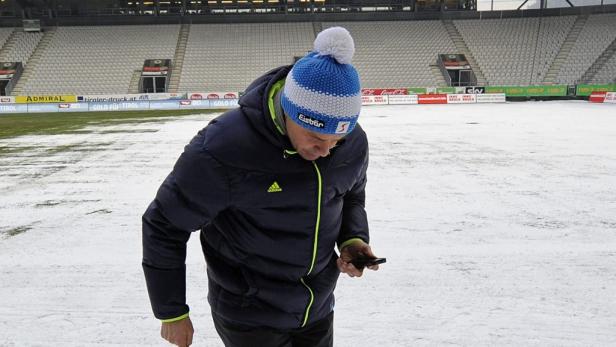 Ein Mann mit Mütze steht in einem verschneiten Stadion und schaut auf sein Handy.