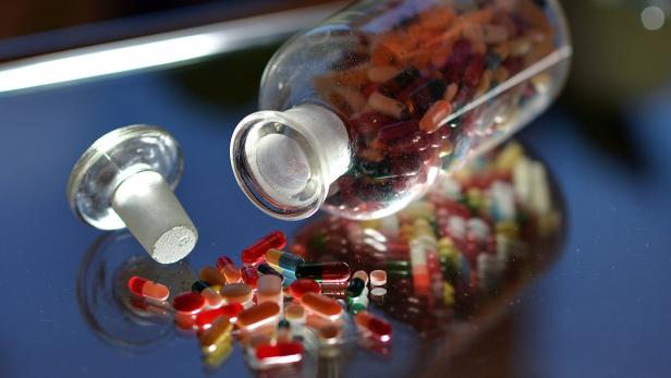 Ein Glasgefäß liegt auf der Seite, einige Pillen sind herausgefallen.