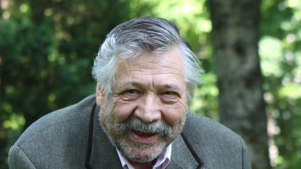 Ein älterer Mann mit grauem Haar und Schnurrbart lächelt in die Kamera.