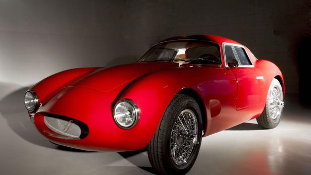 Ein roter Oldtimer mit Speichenfelgen steht in einem Studio.
