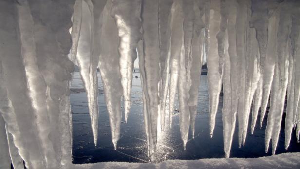 Eiszapfen hängen von einem schneebedeckten Vorsprung und spiegeln sich im Wasser.