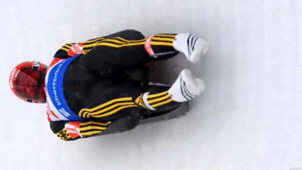 Ein Rennrodler in Schwarz-Gelb liegt auf seinem Schlitten auf dem Eis.