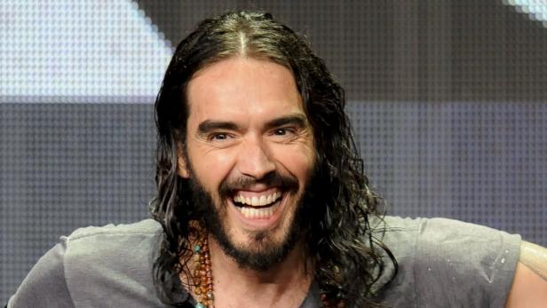 Russell Brand lächelt mit offenem Mund.
