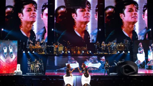 Eine Prince-Tribute-Show mit Musikern und Tänzern auf einer Bühne vor einer großen Leinwand mit Prince.