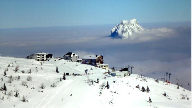 Winterlandschaft mit schneebedeckten Häusern und einem Berg, der aus den Wolken ragt.