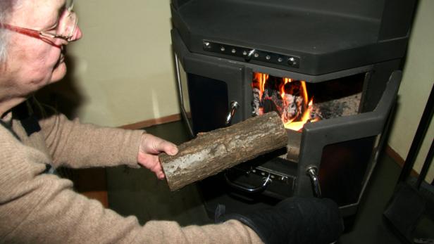 Eine ältere Person legt ein Holzscheit in einen Kamin.