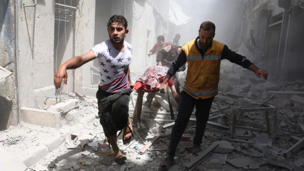 Männer tragen eine verletzte Person durch die Trümmer eines zerstörten Gebäudes.