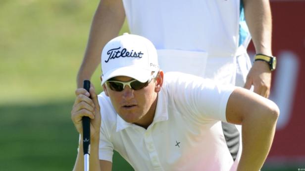 Ein Golfspieler mit Sonnenbrille und Kappe zielt mit seinem Putter auf dem Grün.