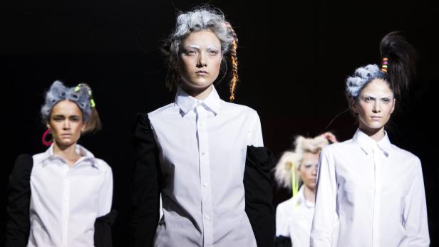 Models präsentieren extravagante Frisuren und schwarz-weiße Kleidung auf dem Laufsteg.
